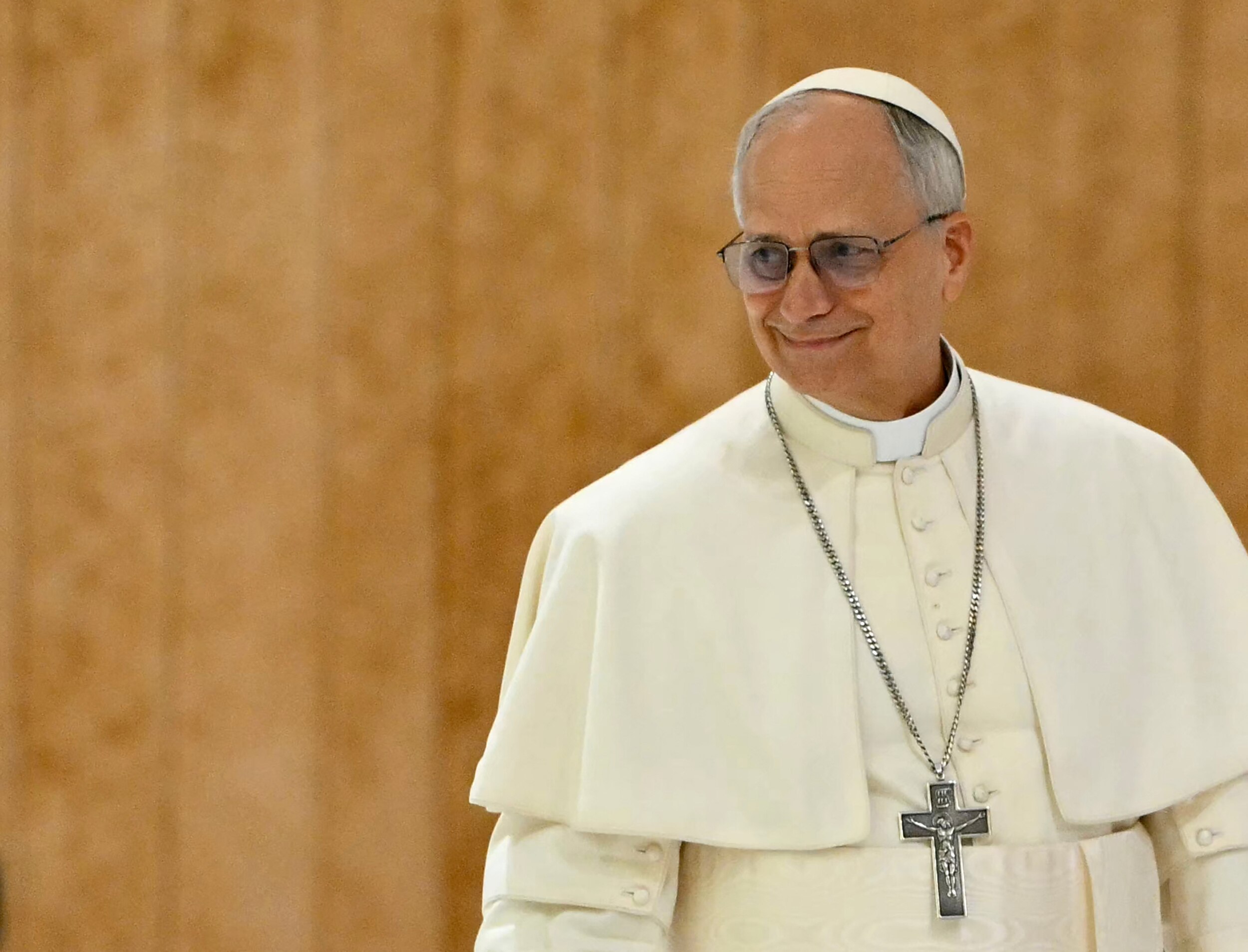 the pope smiles in front of a beige background