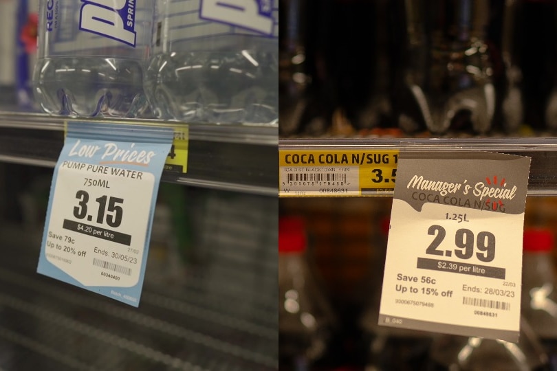 A composite shot of two price tags in a supermarket. One for water reads $3.15 and one for Coke reads $2.99.