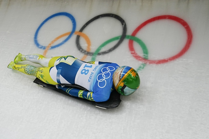 Athlete in yellow and blue outfit slides down an ice ramp at the Winter Olympics skeleton competition