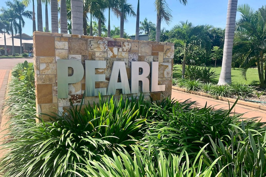 A feature wall outside an aged care facility is seen with the word 'PEARL' written on bricks in a green garden.