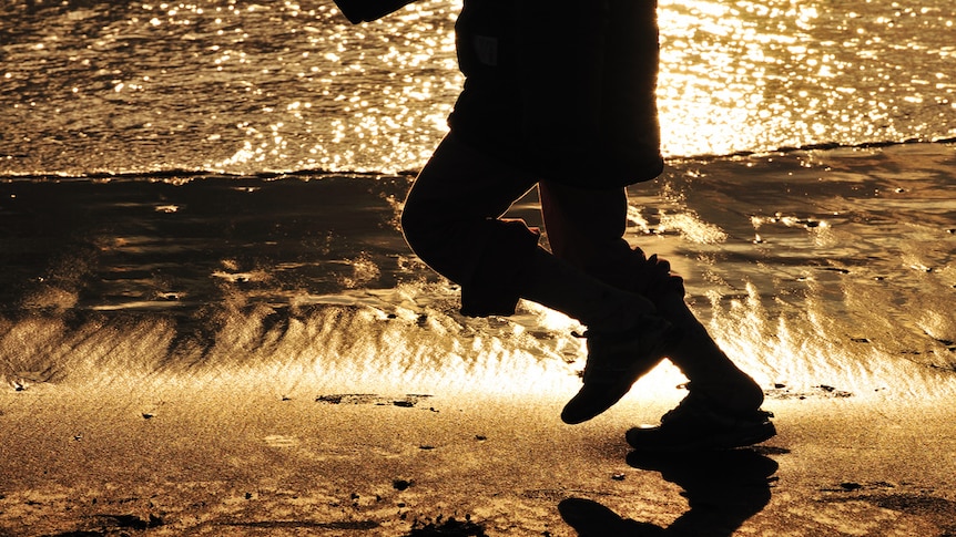 A child's legs seen running on the beach with water behind.