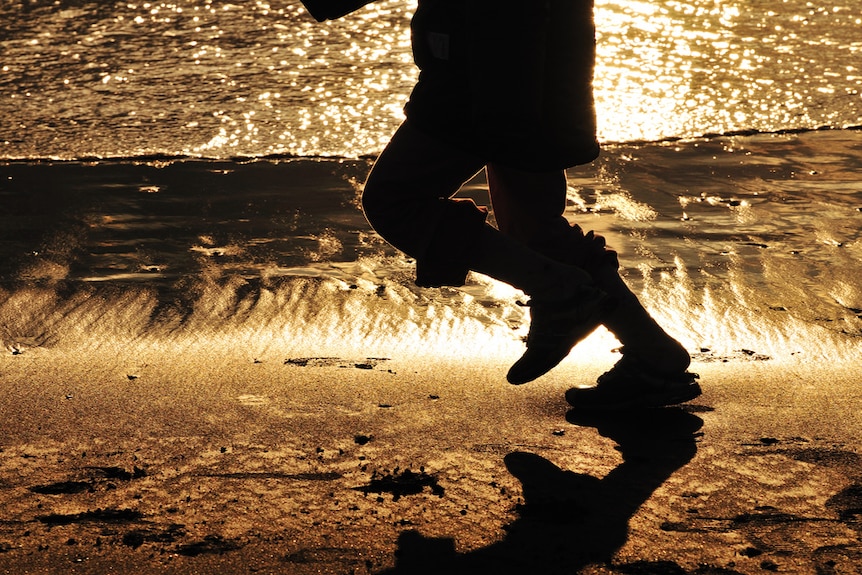 A child's legs seen running on the beach with water behind.