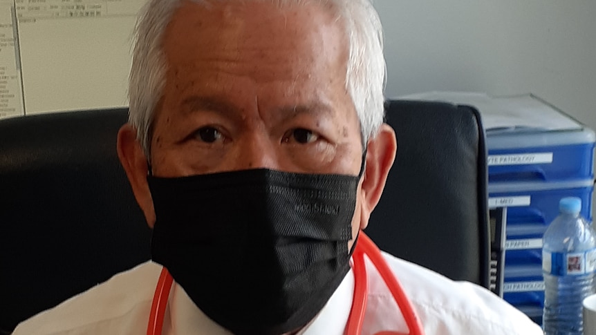 Dr Chung sits at a desk in  black face mask with a stethoscope around his shoulders