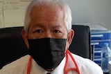 Dr Chung sits at a desk in  black face mask with a stethoscope around his shoulders