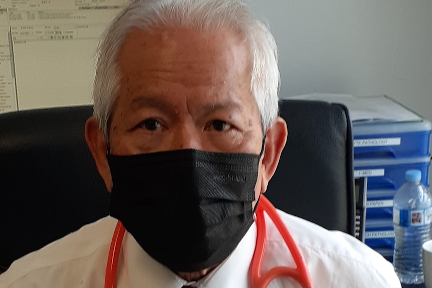 Dr Chung sits at a desk in  black face mask with a stethoscope around his shoulders