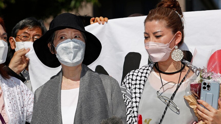 Close up of two masked women standing in front of banner.