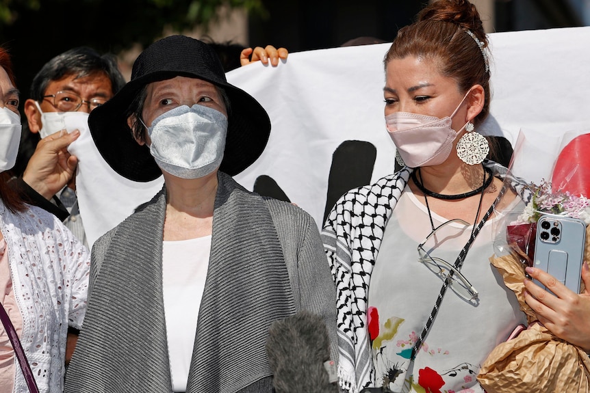 Close up of two masked women standing in front of banner.