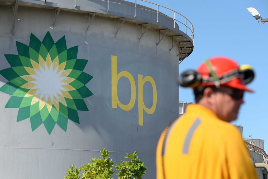 A worker in high-vis and a hard hat stands in front of a large reservoir tower bearing BP branding.