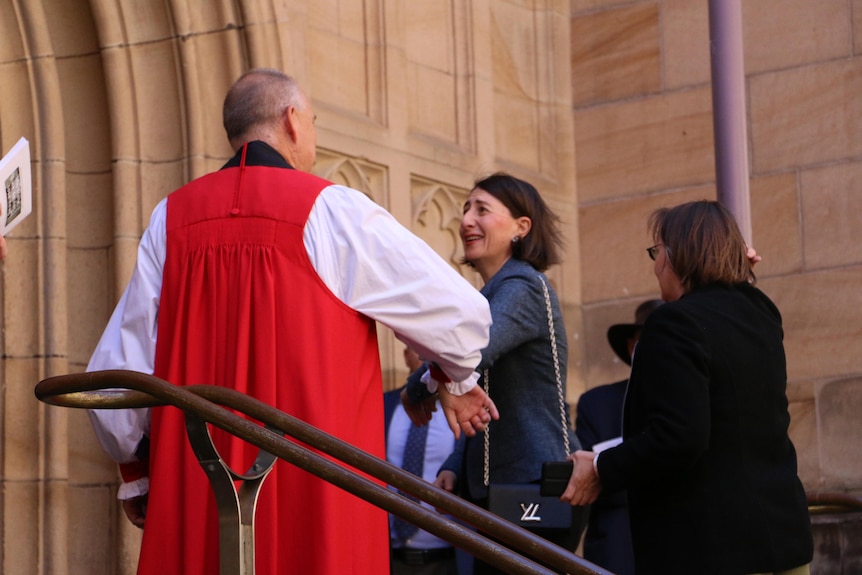 NSW Premier Gladys Berejiklian bumps elbows with a minister as she arrives a church.