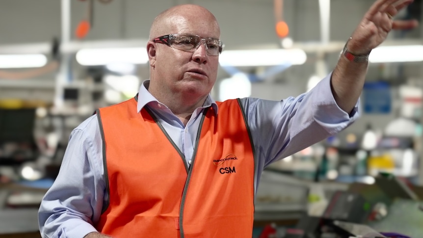 Man wearing a hi-vis orange vest and blue shirt with his left arm up in the air and his head tilted slightly towards it