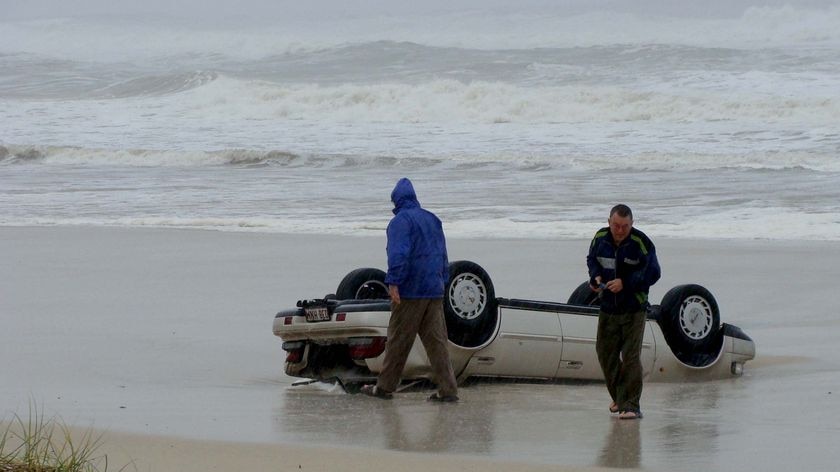 A car lies on the beach after a powerful swell swept it into the ocean