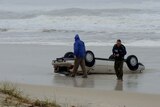 A car lies on the beach after a powerful swell swept it into the ocean