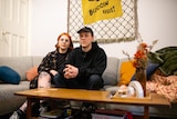 A young man and woman sit on a couch.
