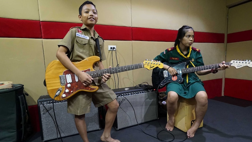 Two Thai teens in scout uniforms strum electric guitars