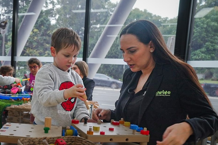 Woman sits playing a puzzle with a young child at an early learning centre.