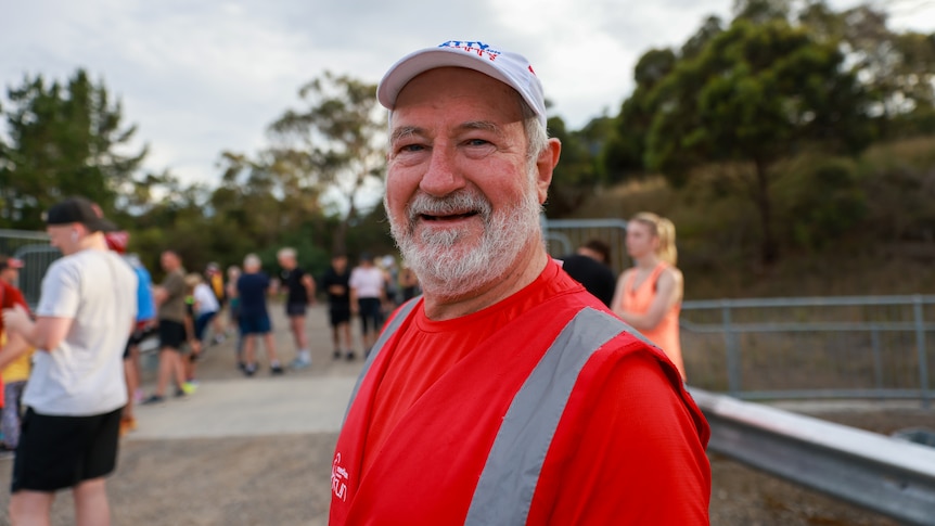 Mike Elder wearing a parkrun volunteer red vest smiling. 