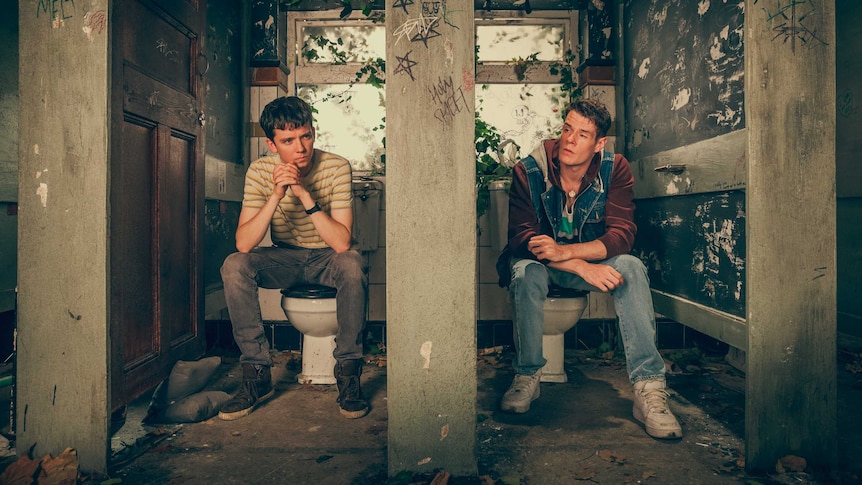 Two teenage boys sitting in rundown toilet stalls