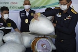 Three people in a room holding a large bag filed with a white substance on a scale 
