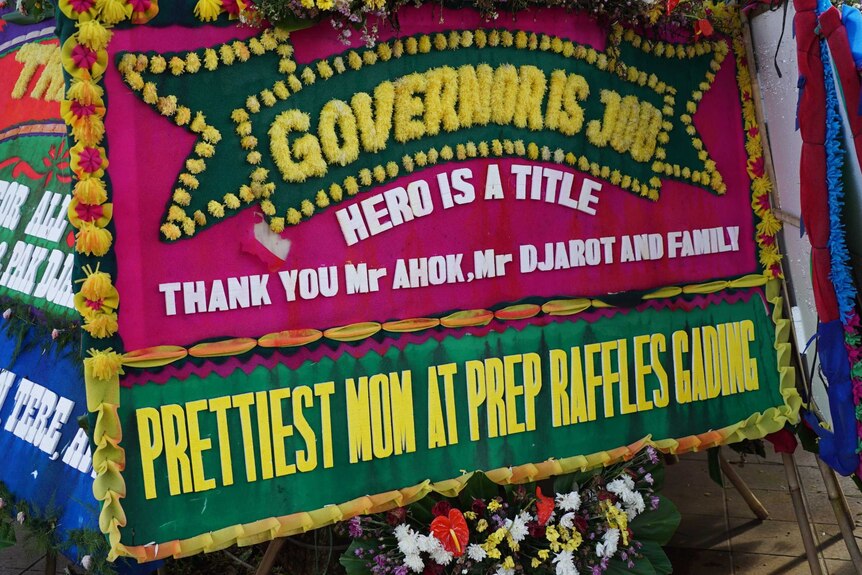 A red and green sign adorned with yellow flowers reads: 'Governor is job, hero is a title' 'thankyou mr ahok, mr djarot"