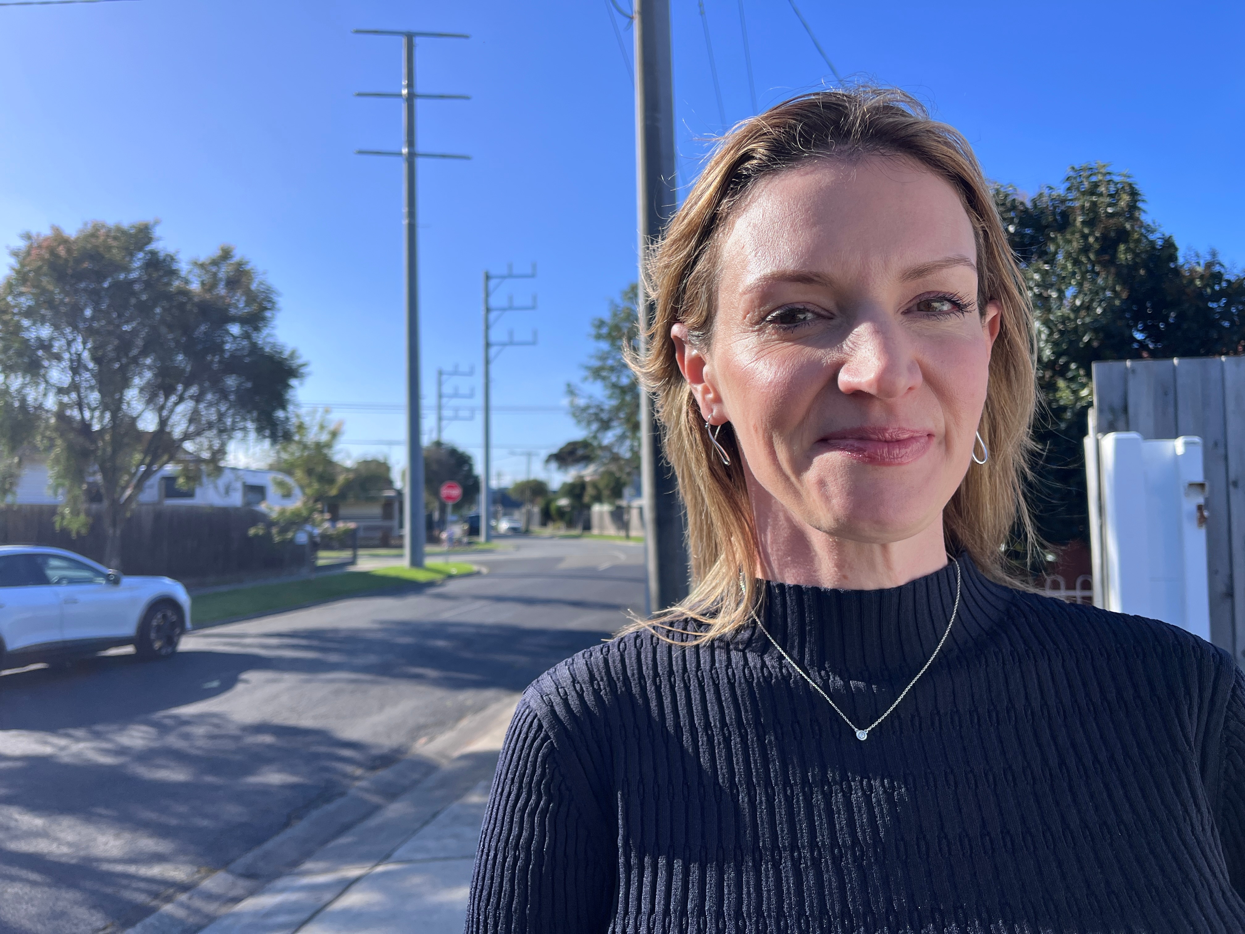 Woman with blonde hair wearing a black jumper standing on a residential street.