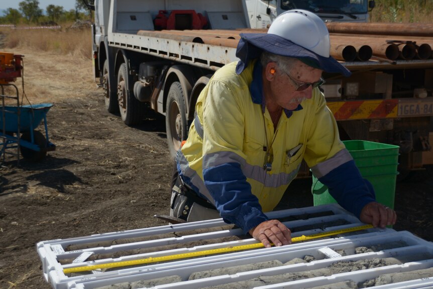 Mine worker measuring drill core samples on table with truck behind him