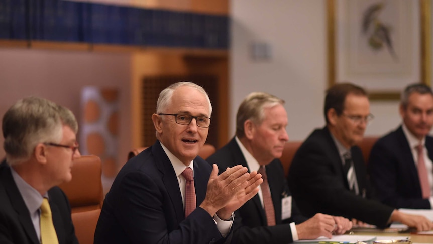Malcolm Turnbull speaks during a COAG meeting, sits with 5 other men in a boardroom.