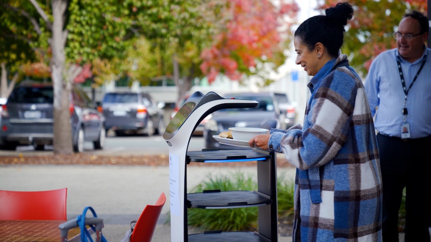 A woman wearing a blue jacket smiles at robot 