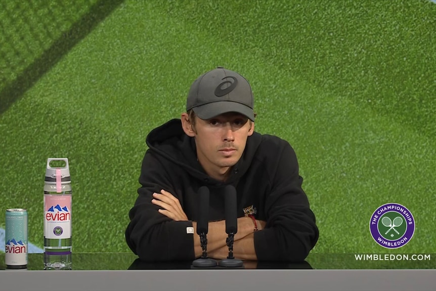 Australian tennis player Alex de Minaur, wearing a black hoodie, sits slumped during a press conference at Wimbledon.