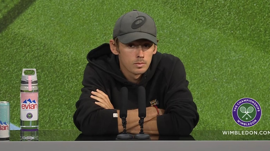 Australian tennis player Alex de Minaur, wearing a black hoodie, sits slumped during a press conference at Wimbledon.