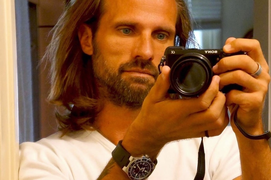 A man with long hair and a beard takes a selfie.