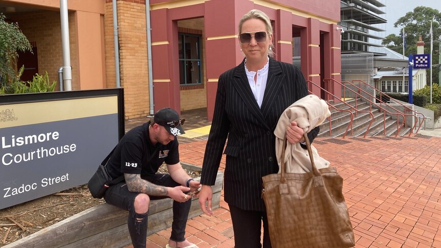 A blonde woman in sunglasses and a black suit stands outside the Lismore Courthouse.