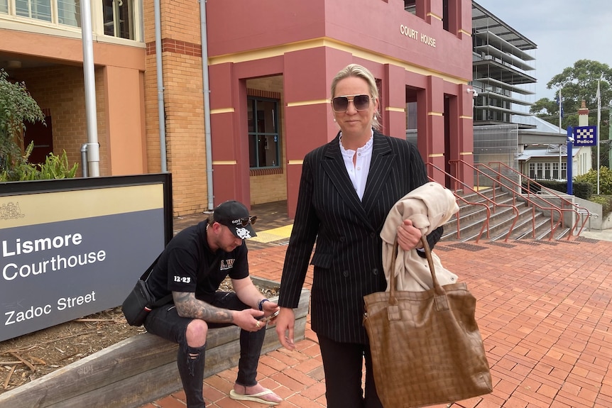 A blonde woman in sunglasses and a black suit stands outside the Lismore Courthouse.