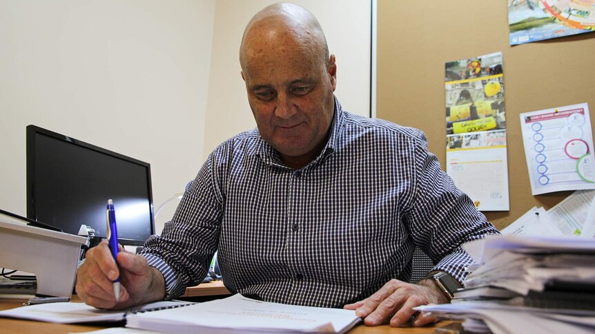 A photo of John Bray as he sits at his desk looking at paperwork.