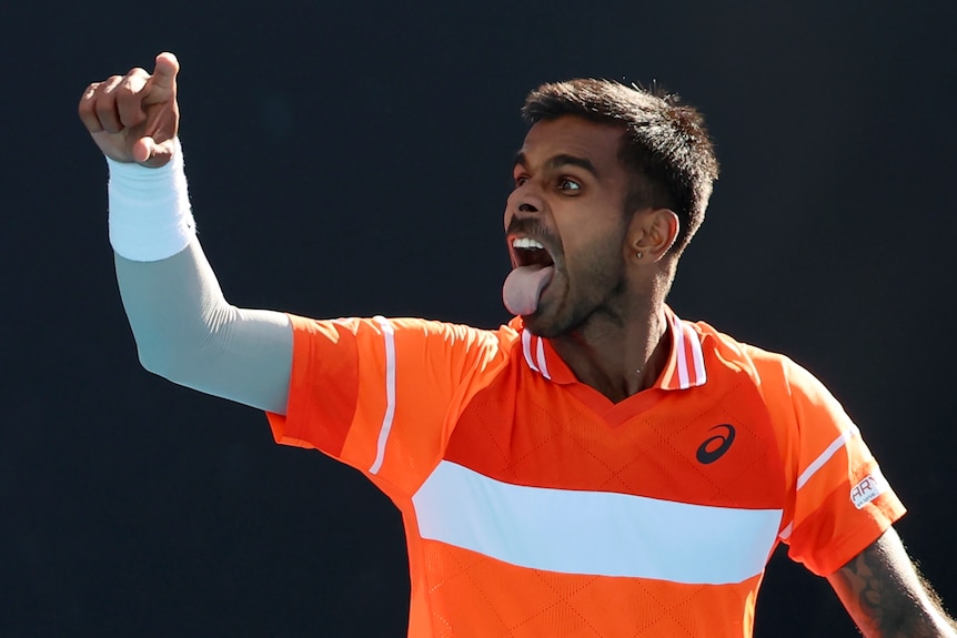 A male Indian tennis player, stickes his tounge out in celebration of a victory