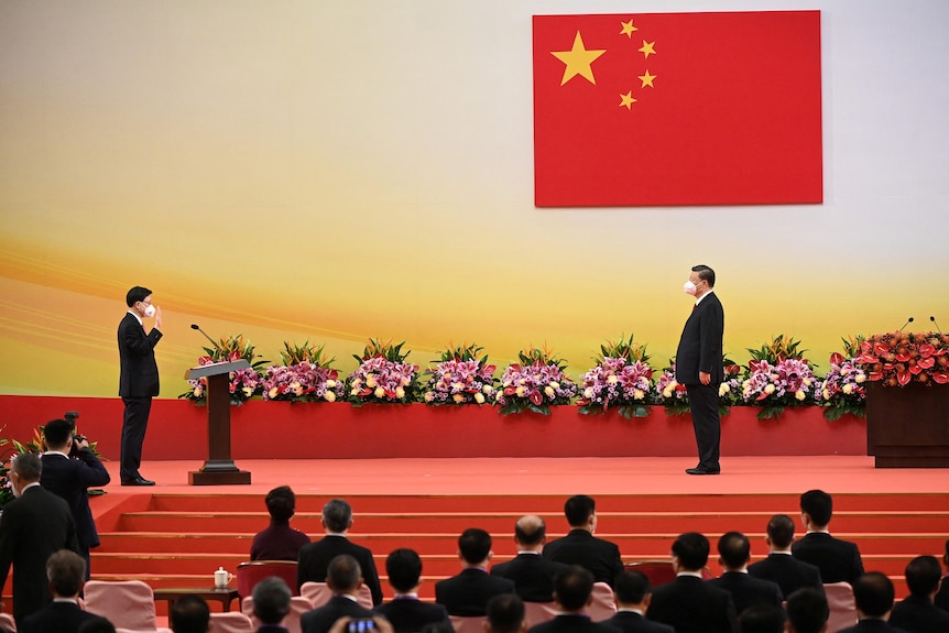 Xi Jinping stands on a stage about three metres from John Lee, who has his hand up