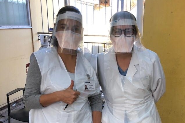 Andrea Mendelsohn looks to the camera as she stands next to another woman. They both wear PPE, Andrea is on the right.