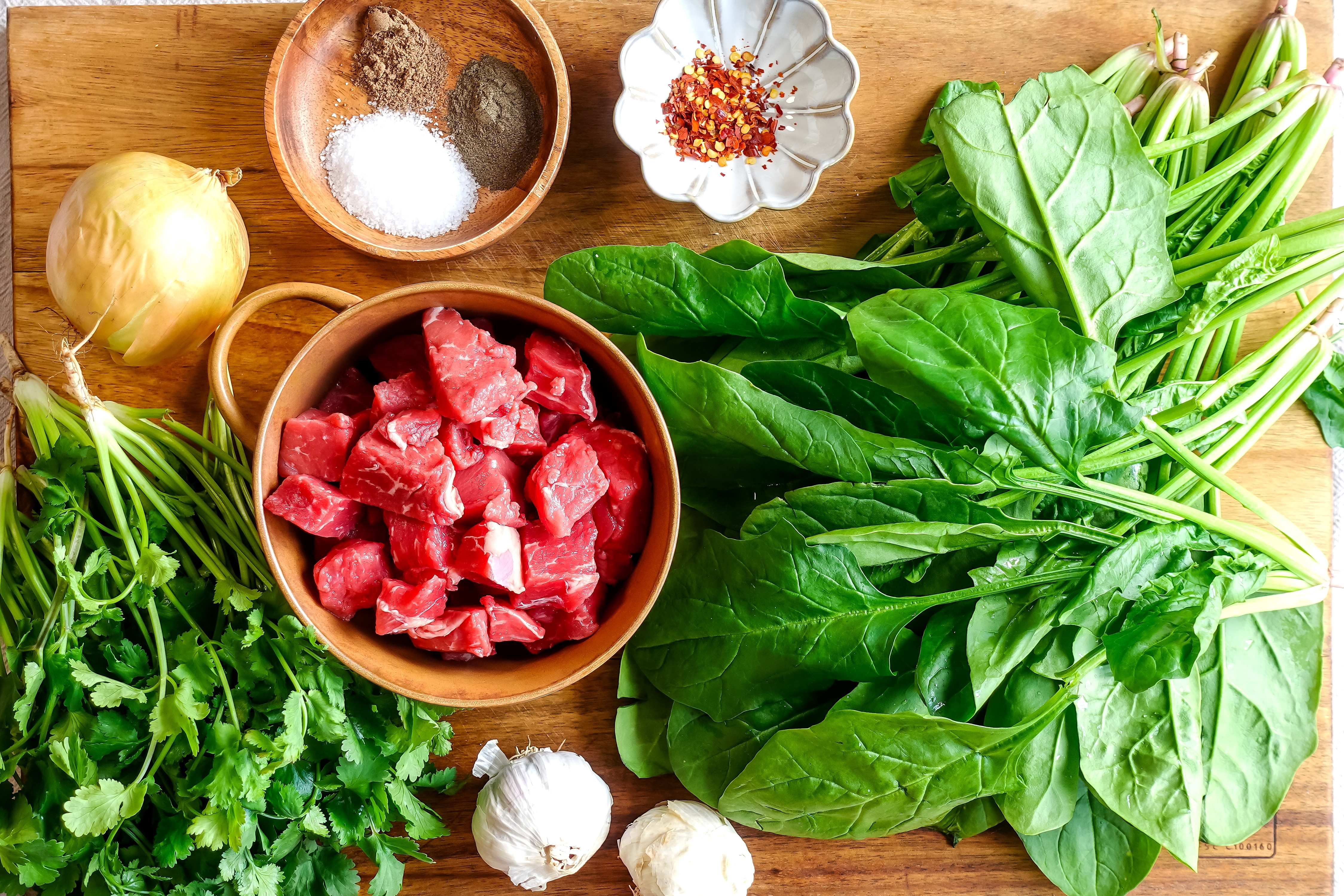 Cubed beef chuck, coriander, garlic, spinach, onion and spices on a chopping board ready to make Lebanese spinach stew with b