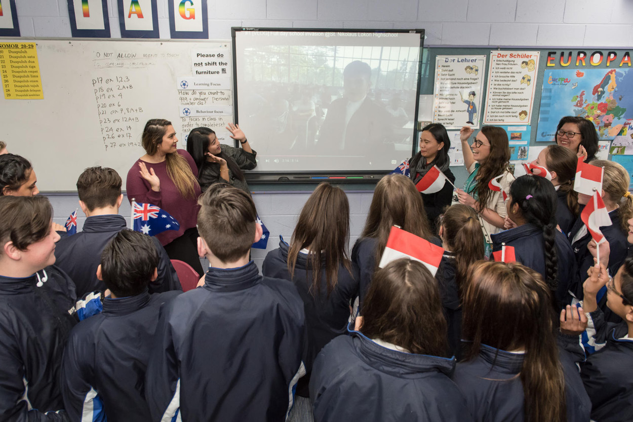 A group of students look at two teachers standing in front of a blackboard 