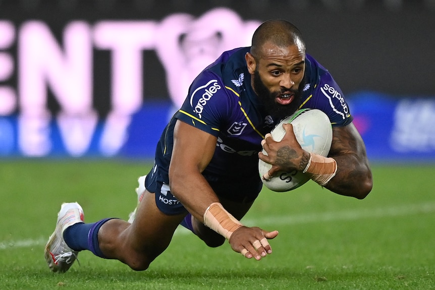 Un jugador del Melbourne Storm NRL se lanza en picado para anotar un try con el balón metido debajo del brazo derecho.