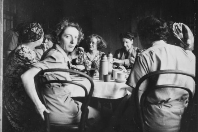 Black and white photograph of women sitting around table with one turned around to face the camera