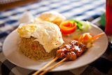 Fried rice dish on a plate served with fried egg and chicken skewers