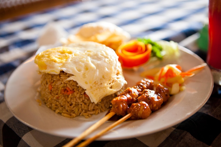 Fried rice dish on a plate served with fried egg and chicken skewers
