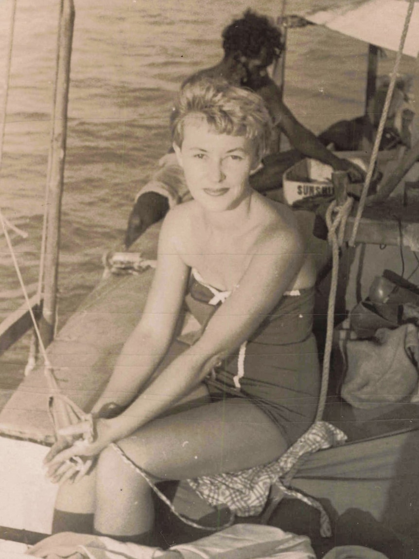 Young blond woman in one-piece swimsuit standing on a boat.