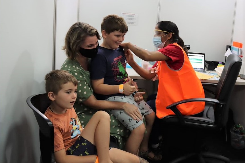 a mum with her two boys. one is getting vaccinated by a health worker