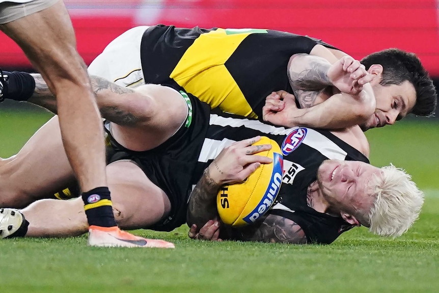 Jordan De Goey grimaces as he hits the ground, while Trent Cotchin completes the tackle