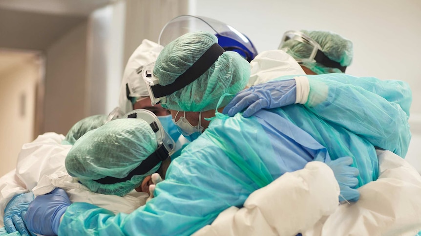 A group of doctors in full surgery scrubs gear are hugging in a circle