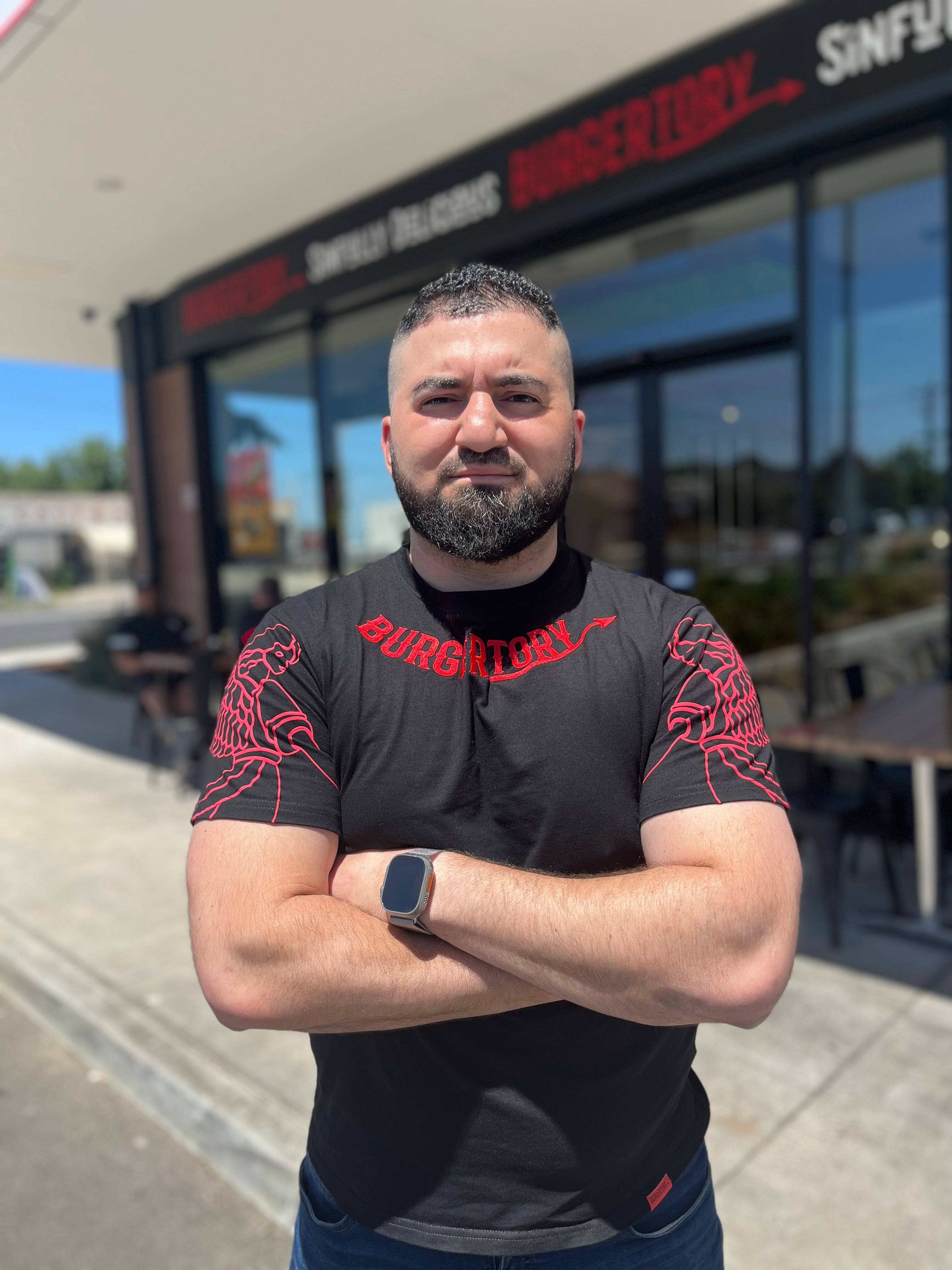 Man wearing a black shirt that says 'Burgertory' on the collar, with his arms folded.
