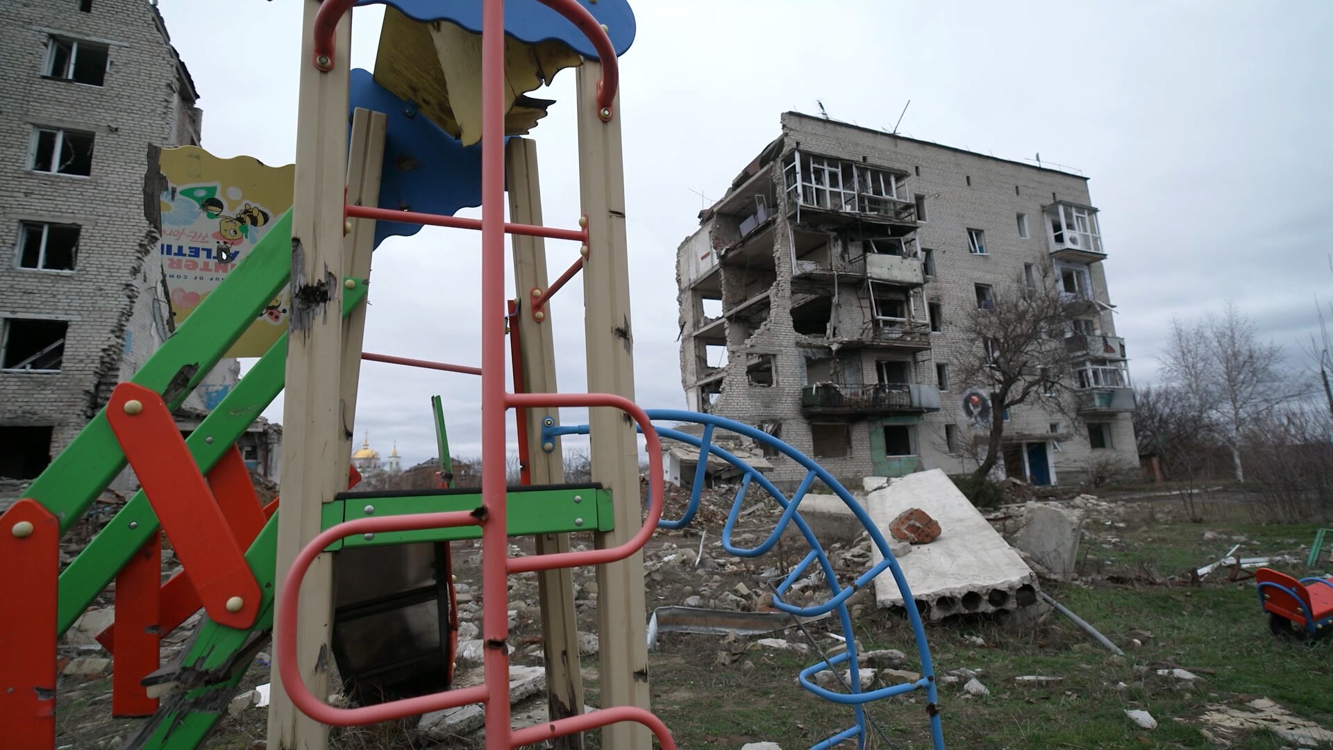 A severely damaged building with a playground equipment in the foreground.