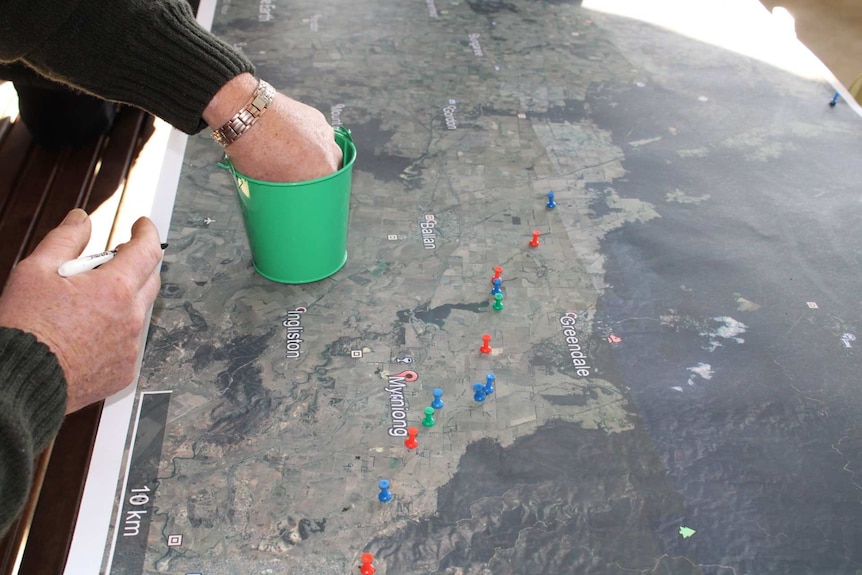A hand sticking coloured pins into a map