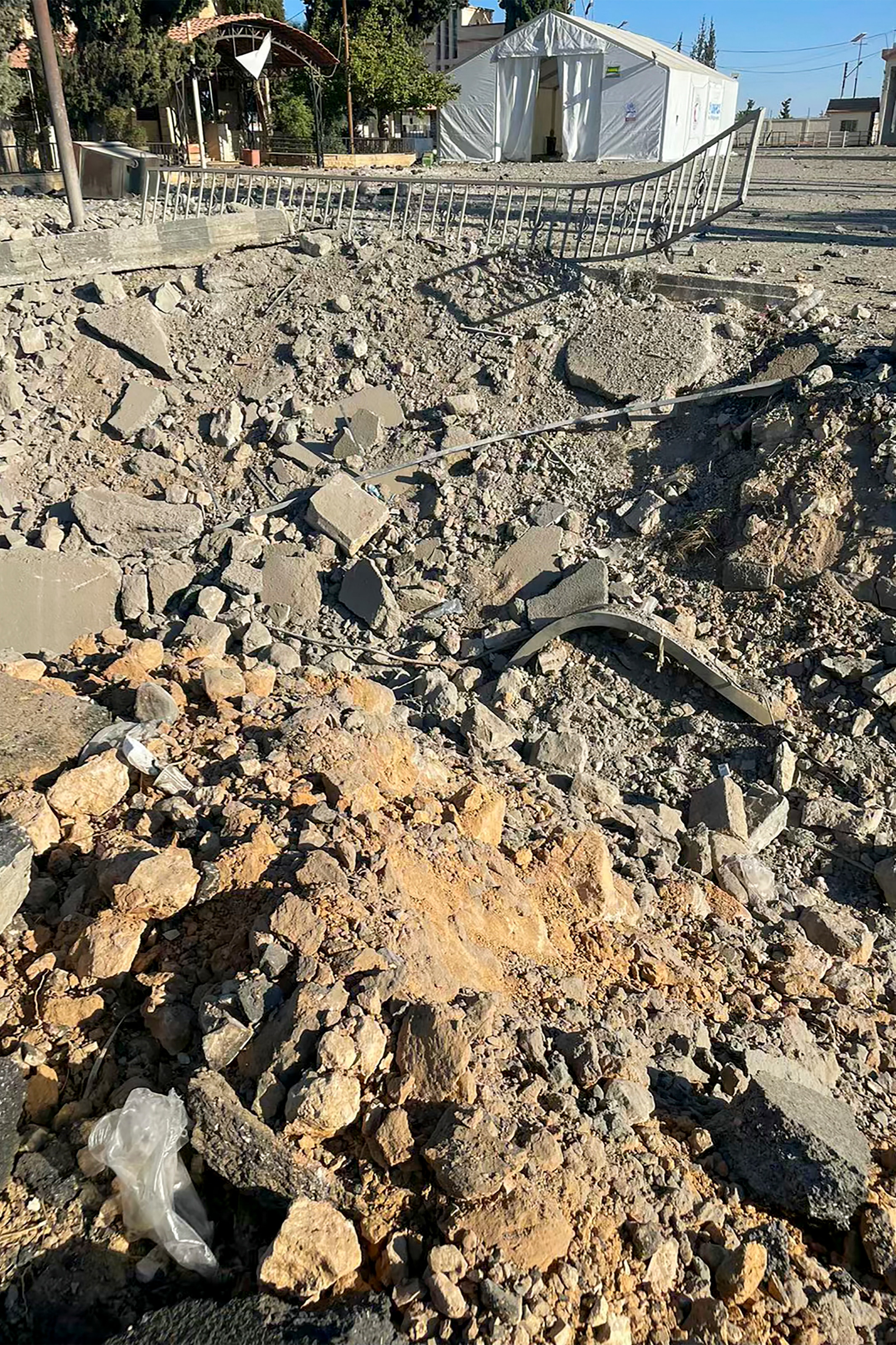 A hole in the ground with rubble in it, next to a white building.